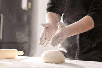Baker sprinkling flour over dough on kitchen table