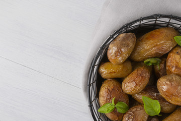 Baked potatoes in a black basket.  The background is white. Copy space. Top view. Horizontal shot.