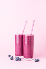 Two glasses of blueberries smoothie with straws on pink background. Healthy summer drink.