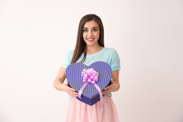 Beautiful young woman with gift box on light background