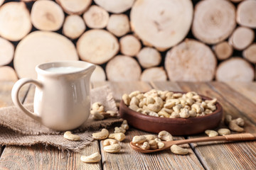 Plate with tasty cashew nuts and jug of milk on wooden table