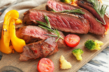 Wooden board with meat and vegetable garnish on table, closeup