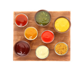 Bowls with different sauces on wooden board, isolated on white