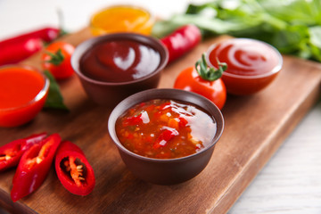 Bowls with different sauces and ingredients on wooden board, closeup