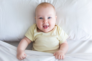 top view of cute smiling little baby girl lying on the bed under blanket © Di Studio
