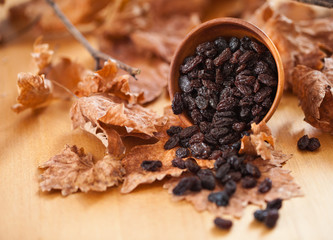Black raisins in a wooden bowl. On dry leaf and brown wooden background.