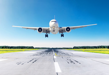 Obraz premium Samolot pasażerski z jasnymi światłami do lądowania, lądujący przy dobrej pogodzie z błękitnym niebem na pasie startowym.