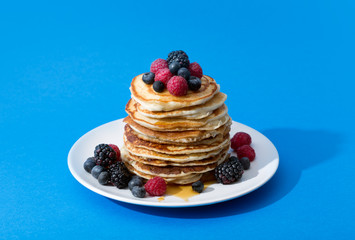 Pancakes with berries and honey on the blue background