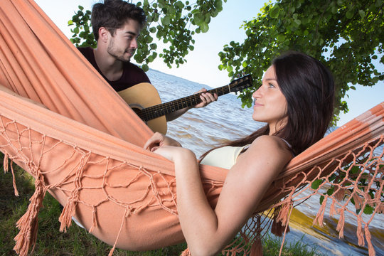 beautiful girl relaxing in hammock listening her boyfriend playing guitar