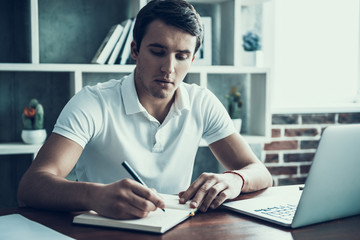 Young Businessman Writing Notes and Using Laptop.