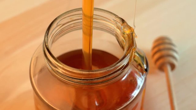 Pouring honey into glass jar onwooden background, close up