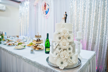 Close-up photo of big white wedding cake decorated with fondant flowers and two figures on top.