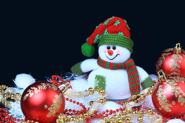 Toy snowman with a red festive balls and decorations, in the black background