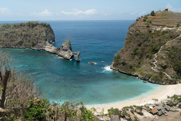 Beach with with azure water, rocky mountains and clear water at sunny day. Clear blue ocean waves rolling to the beach. Nusa Penida, Bali, Indonesia. Travel concept.