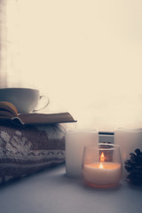 Details of still life in the home interior. Sweater, cup, wool, cozy, book, candle. Moody. Cosy autumn winter concept. Copy space