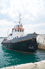 Black tugboat moored in the sea port.