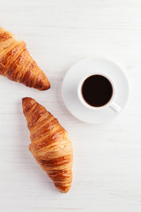 A cup of coffee and two croissants on white wooden table. Traditional french breakfast. Top view.