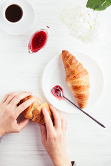 Coffee, croissants, jam on white wooden table. Traditional french breakfast. Woman's hands holding croissant. Top view.