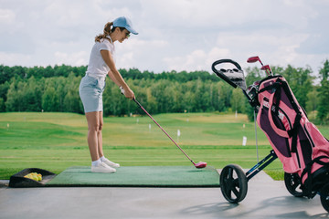 Obraz premium side view of woman in polo and cap playing golf at golf course