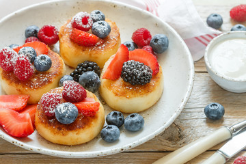 Cottage cheese pancakes, syrniki, curd fritters with fresh berries (raspberry, strawberry, blueberry, BlackBerry) and powdered sugar in a white plate