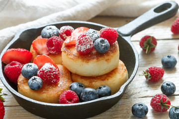 Cottage cheese pancakes, syrniki, curd fritters with fresh berries (raspberry, strawberry, blueberry, BlackBerry) and powdered sugar in a cast iron pan