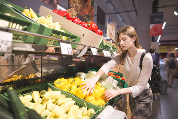 Portrait of a stylish girl who buys peppers in the vegetable department of the supermarket. Attractive woman buys vegetables in the store. Purchase of products in the supermarket.