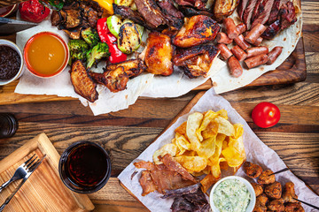 Grilled assorted food set on wooden background. Top view dishes of grilled chicken, potato, cola, sausage.