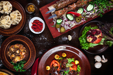 Aassorted traditional Georgian food on a wooden background and rustic plates. Top view of khinkali, shish kebab, mushrooms on the grill.