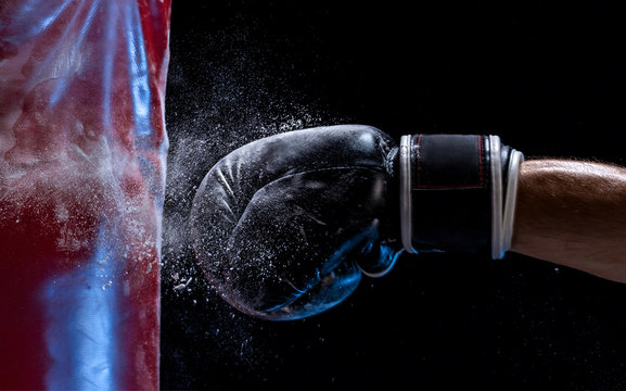 Close-up Hand Of Boxer At The Moment Of Impact On Punching Bag Over Black Background