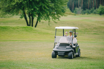 Woman in cap riding golf cart at golf course on summer day