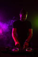 Fototapeta na wymiar Attractive young DJ playing on turntables with color light effects