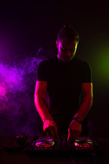 Attractive young DJ playing on turntables with color light effects