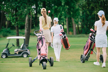 back view of women with golf gear walking on green lawn at golf course