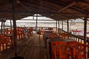 Interior view of a local beach restaurant with plastic chairs thatched roof and wooden floor with view of the sea beach at Talsari West Bengal, India.