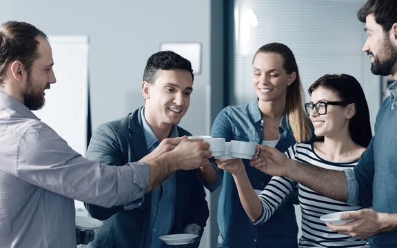 Friendly team. Cheerful smiling young colleagues having a break in the office while drinking coffee and expressing positivity