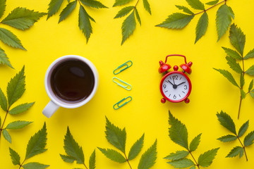 Business concept. Coffee Cup and clock alarm Clock on yellow background with plant leaves.