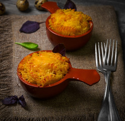 Two ceramic coconut frying pan with baked in the oven pasta with cheese. Ingredients for baked pasta Parmesan cheese, quail eggs, basil, spinach. Gray wooden vintage rustic background.