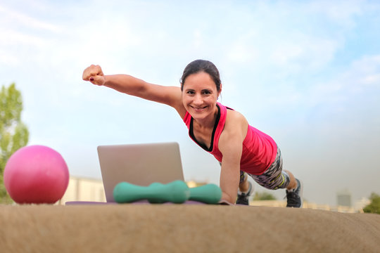 fit woman watching online fitness program and doing workout infront of a laptop on a mat