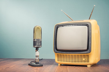 Retro old outdated yellow TV receiver from circa 70s and studio microphone on wooden table front...