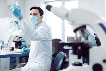 Biological engineering. Smart pleasant intelligent scientist standing in the lab and holding a test...