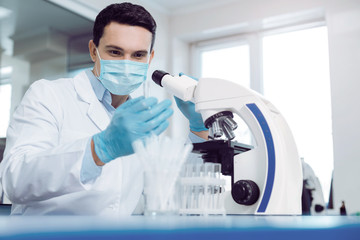 Modern research. Professional smart male scientist wearing uniform and looking at the test tube...
