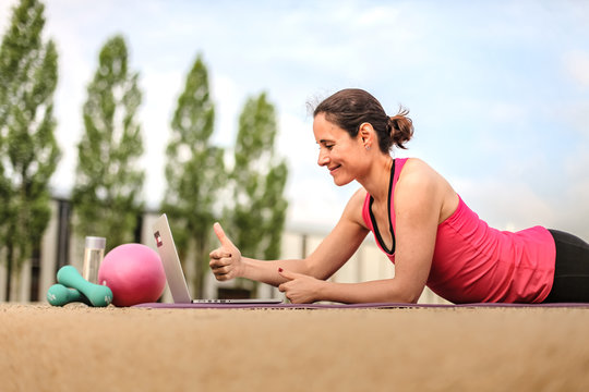 female fitness coach making  thumbs up infront of a laptop after an successful online workout  on a mat 