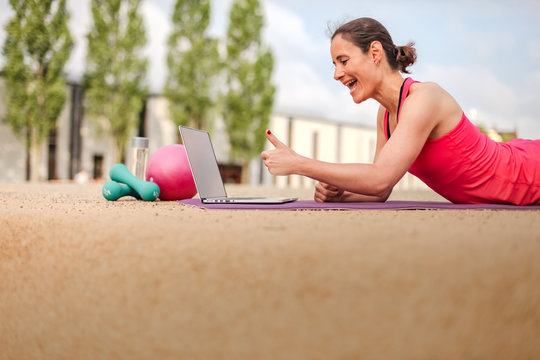 female fitness coach making  thumbs up infront of a laptop after an successful online workout  on a mat 