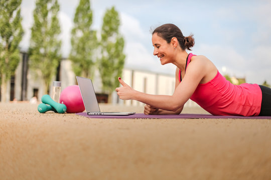 female fitness coach making  thumbs up infront of a laptop after an successful online workout  on a mat 