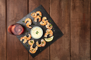 Overhead photo of shrimps on a dark rustic background, with a sauce and a glass of rose wine, with place for text