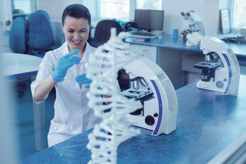 Genetic discovery. Happy delighted positive woman smiling and looking at the test tube while making a genetic discovery