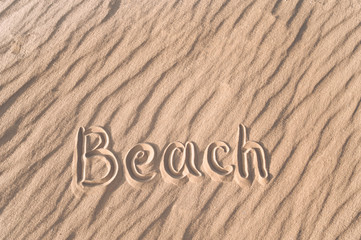 Naklejka na ściany i meble The word beach is written on the sand by hand. Beach season. Postcard. Shadows on the sand.