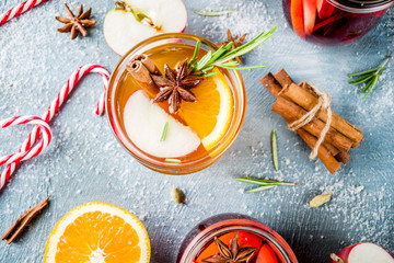 Traditional winter drinks, white and red mulled wine cocktail,  with white and red wine, spices, apple, orange. On a light blue table,