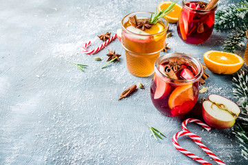 Traditional winter drinks, white and red mulled wine cocktail,  with white and red wine, spices, apple, orange. On a light blue table,