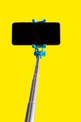 Monopod for selfie with smart phone. Selfie stick with smartphone isolated on yellow background